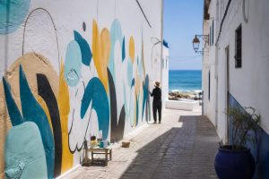 Ruelle blanche ornée d’une fresque et ouverte vers la mer à Asilah