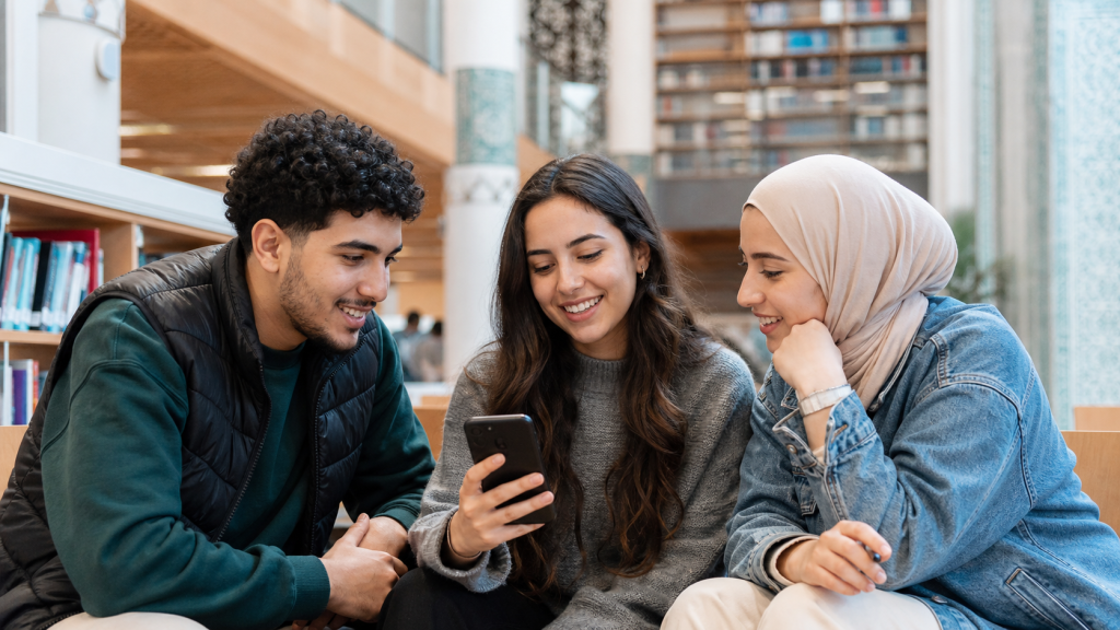 Trois jeunes adultes marocains consultant ensemble un téléphone dans une bibliothèque contemporaine