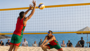 Two Moroccan beach-volleyball players in red and green defending a ball at the net