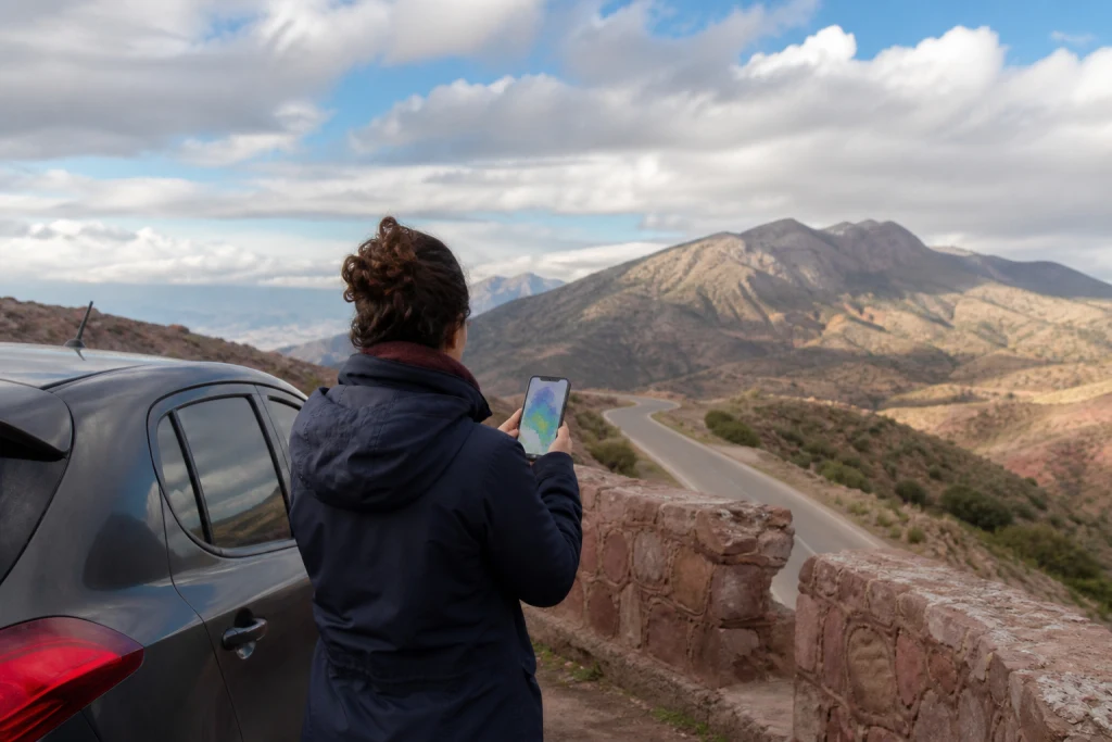 Voyageuse consultant une carte météo sur téléphone avant une route marocaine sous un ciel changeant