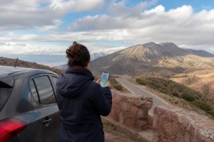 Voyageuse consultant une carte météo sur téléphone avant une route marocaine sous un ciel changeant