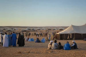 Grand espace de rencontre saharien à Tan-Tan avec tentes traditionnelles, cavaliers lointains et groupes réunis sans scène spectaculaire