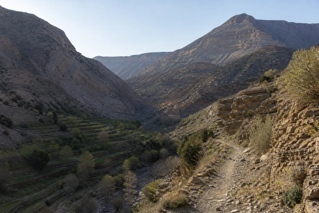 Vallée minérale du Haut Atlas central traversée par un sentier entre cultures en terrasses et formations rocheuses