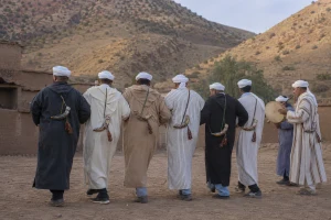 Danseurs adultes de Taskiwin en ligne avec petits Tiskt décorés, tambourin et flûte devant le Haut-Atlas occidental