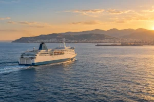 Illustration d’un ferry non identifié naviguant vers une côte méditerranéenne, sans représenter un trajet GNV précis